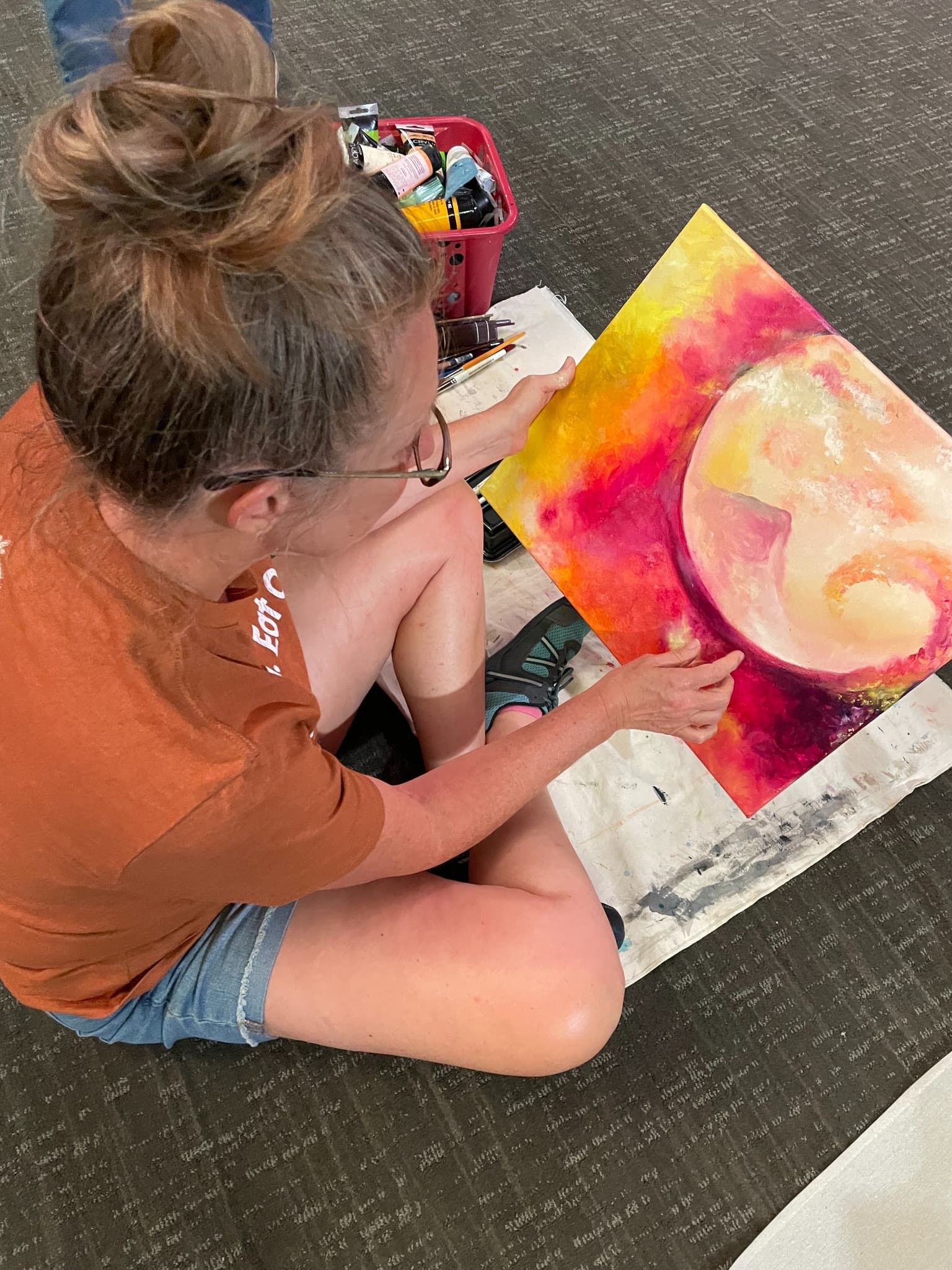 Heather sitting on the floor painting, surrounded by art supplies