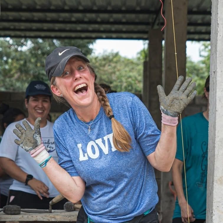 Heather raising her work-gloved hands, wearing a LOVE shirt at a building project