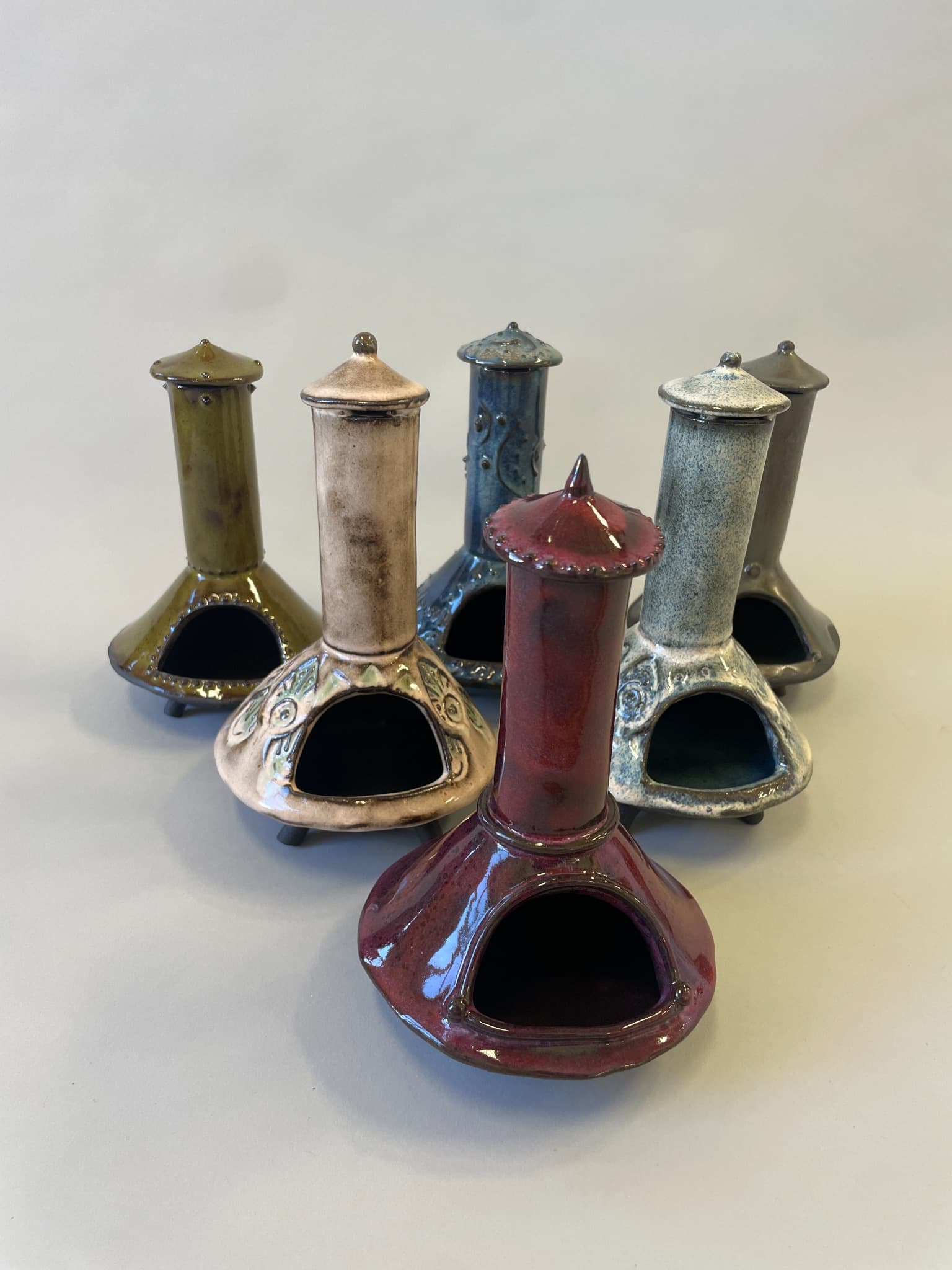 A group of six glazed ceramic chimeneas in varied colors.