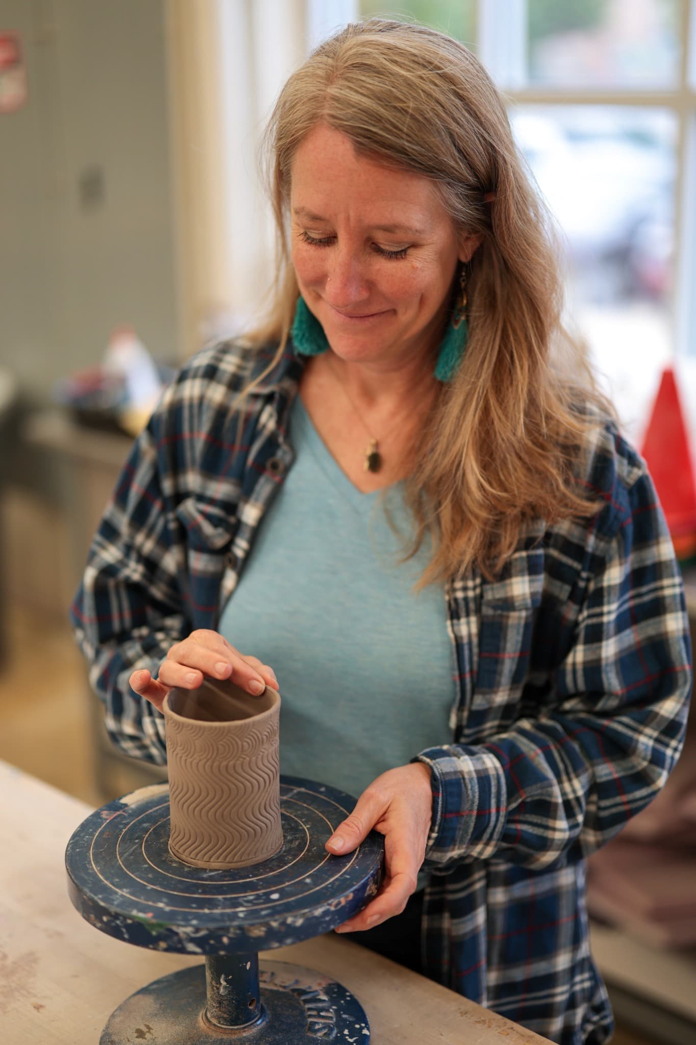 Heather shaping a textured clay vessel on a banding wheel.