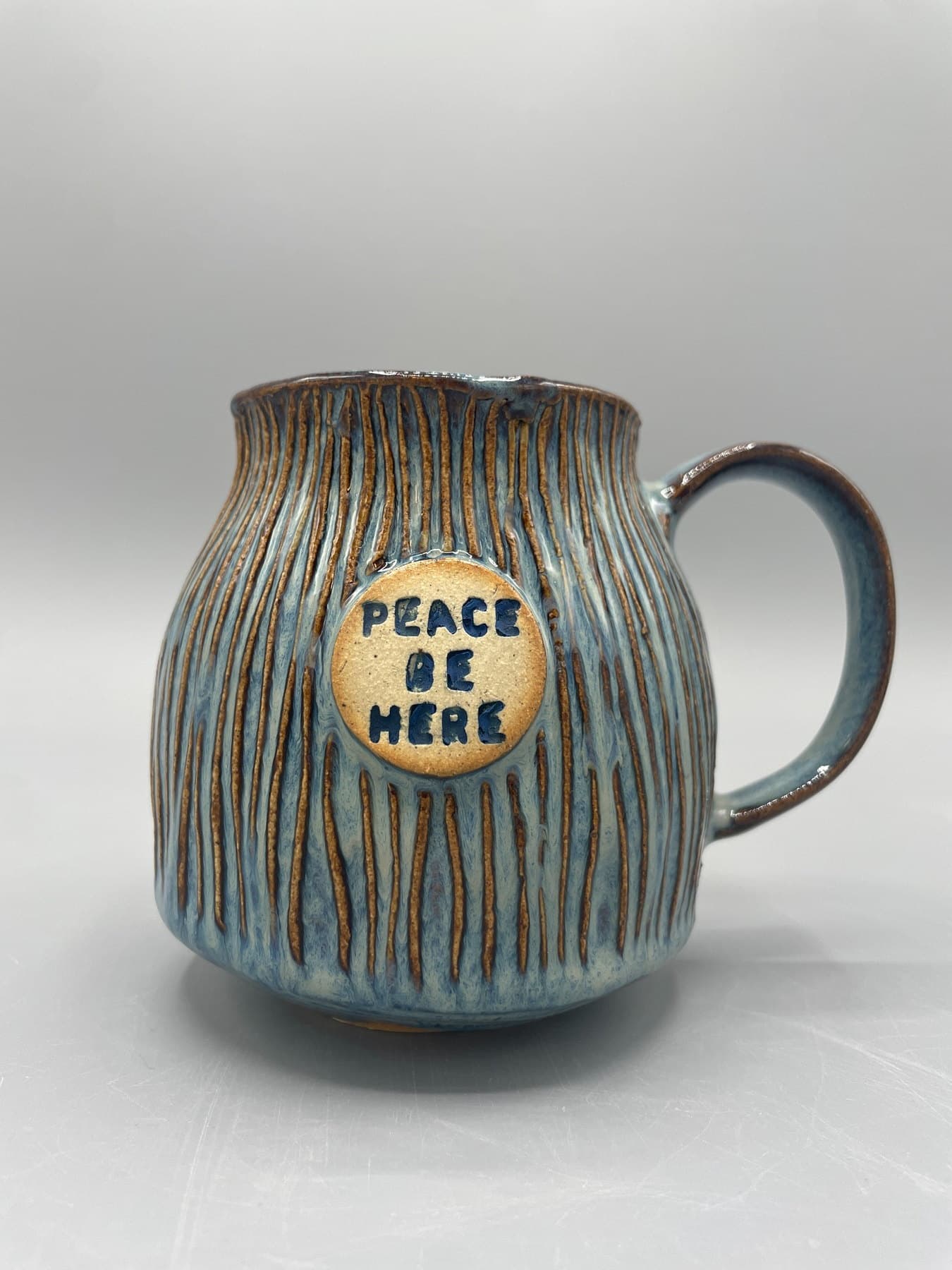 Blue-gray textured ceramic mug with a medallion reading Peace Be Here.