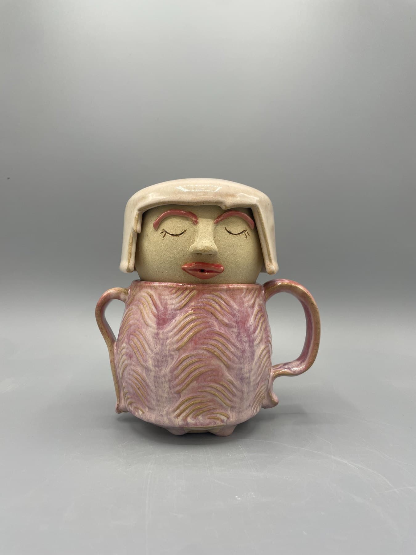 Pink and cream figurative ceramic tea companion with a serene face and two handles.