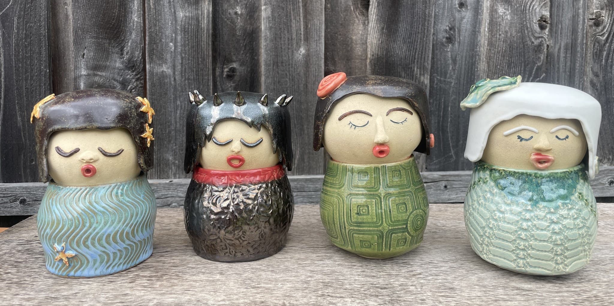 Four handmade ceramic Tea Companions with varied glazes, textures, and peaceful expressions.