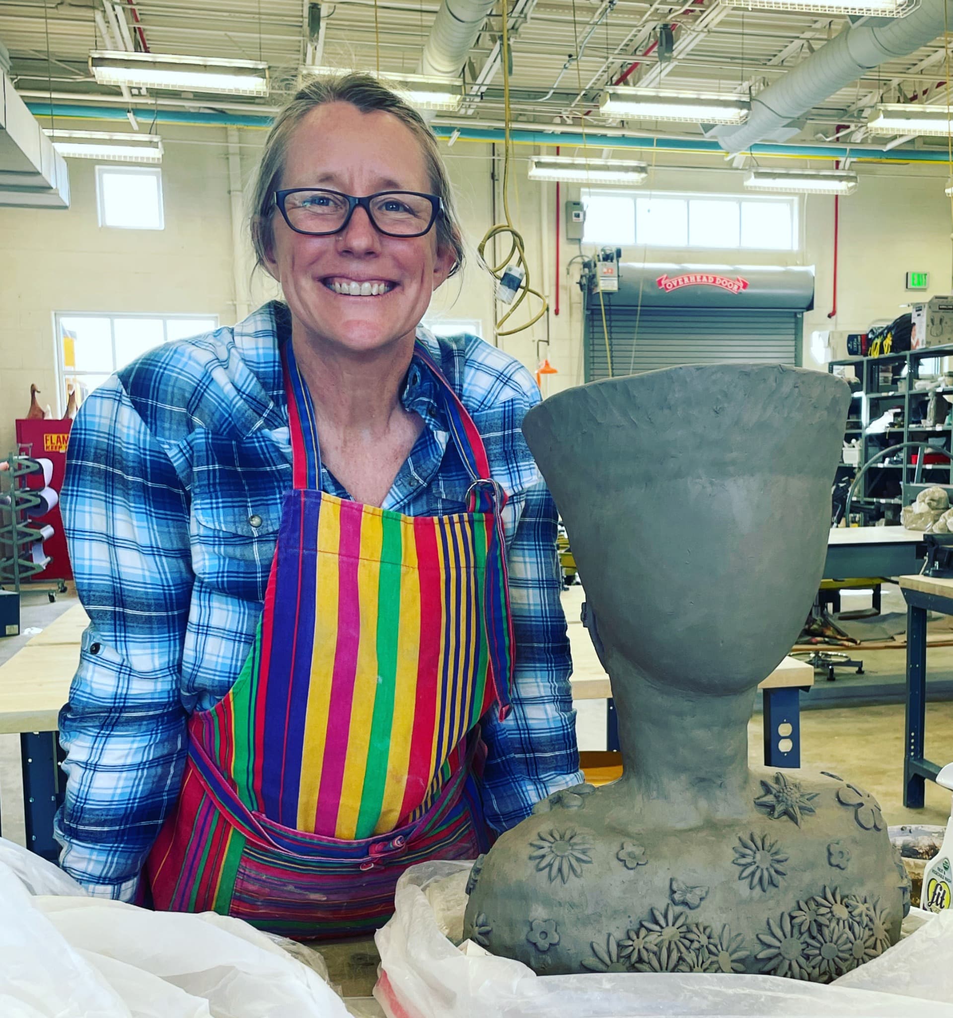 Heather in her working studio beside a large clay bust decorated with flowers.