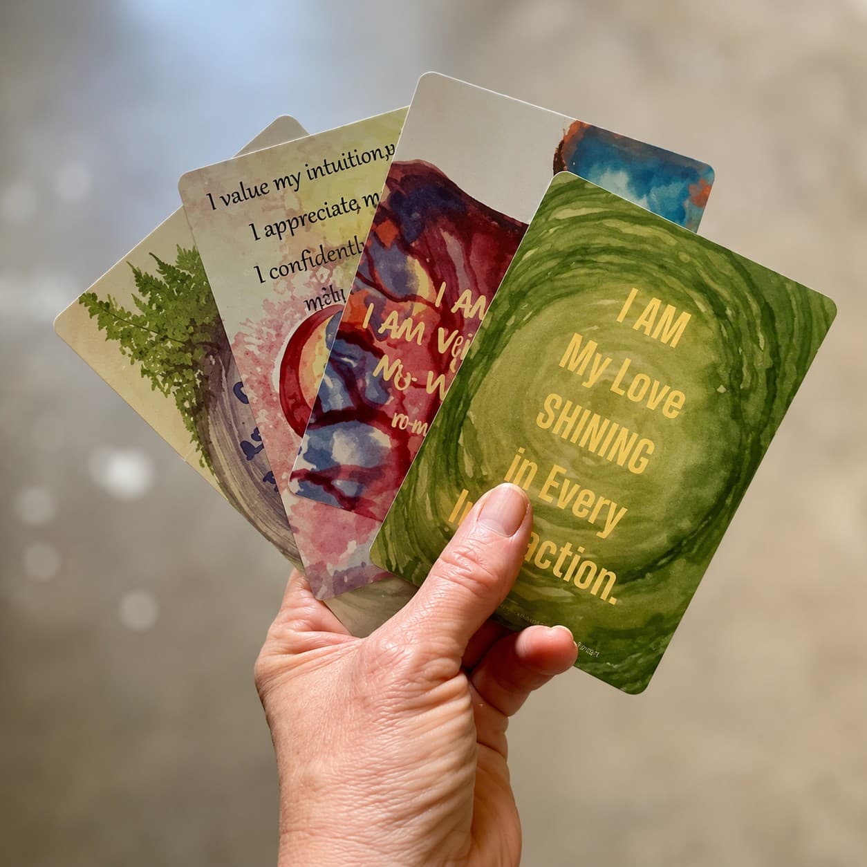 A hand holding a fan of colorful affirmation cards.