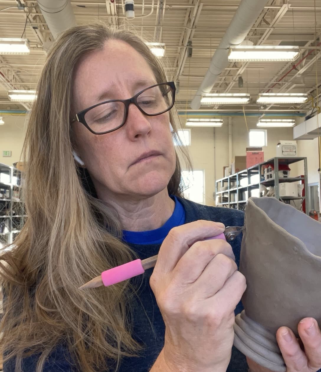 Heather concentrating as she works with a hand tool on a raw clay vessel.